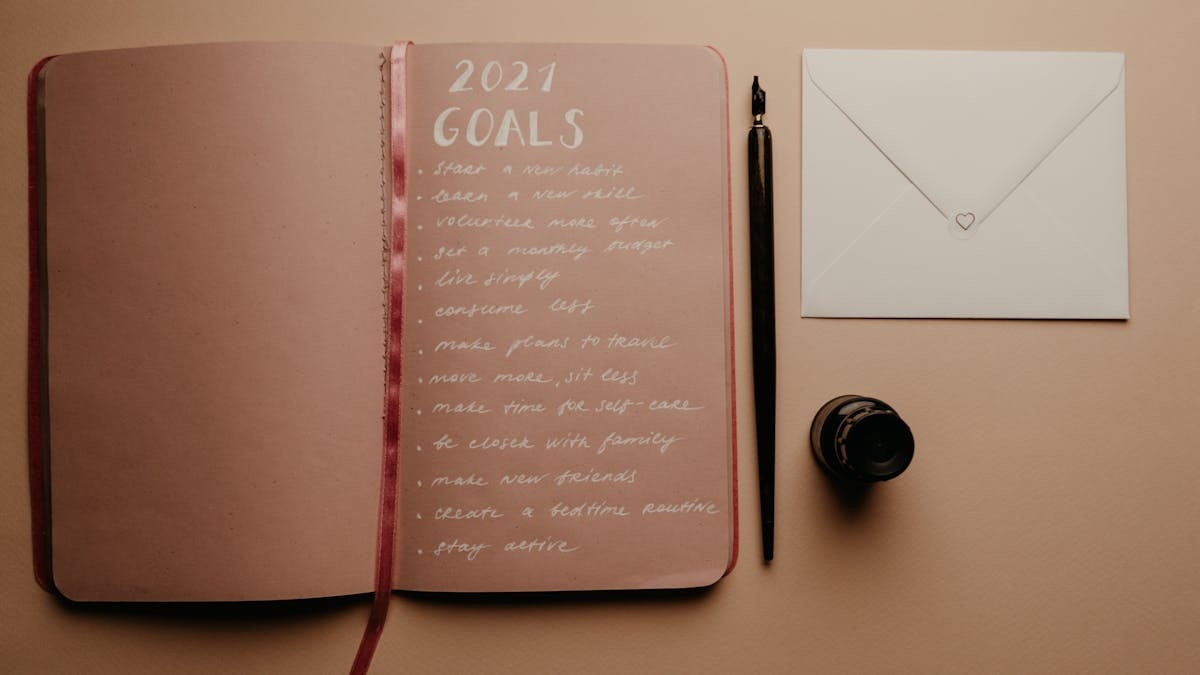 Open notebook with 2021 goals, calligraphy pen, envelope, and ink jar on neutral background.